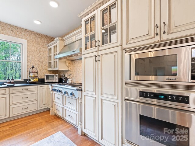 62 Blair Athel Pt, Waynesville, NC 28786 - kitchen with cream cabinets, stainless steel appliances, range hood, dark countertops, and light wood finished floors