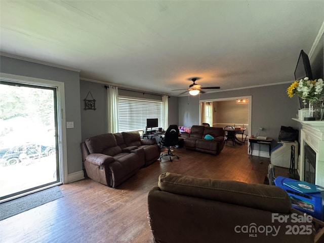 living area featuring wood finished floors, a ceiling fan, ornamental molding, a glass covered fireplace, and baseboards