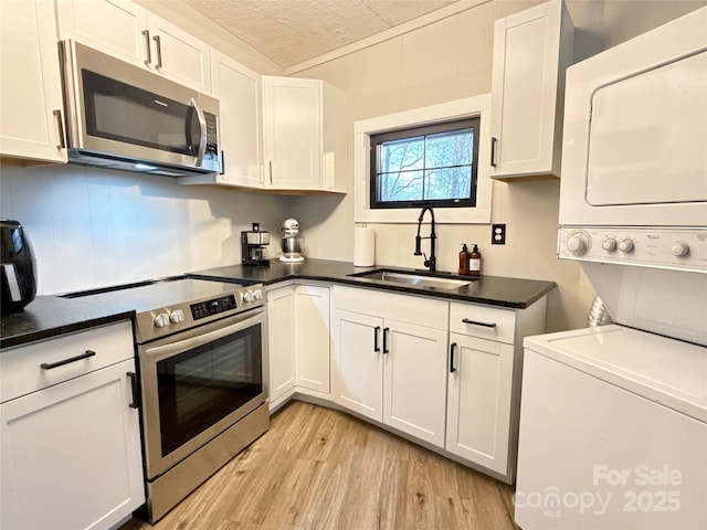 109 Beechwood Ln, Beech Mountain, NC 28604 - kitchen featuring appliances with stainless steel finishes, stacked washing machine and dryer, a sink, light wood-style flooring, and white cabinets