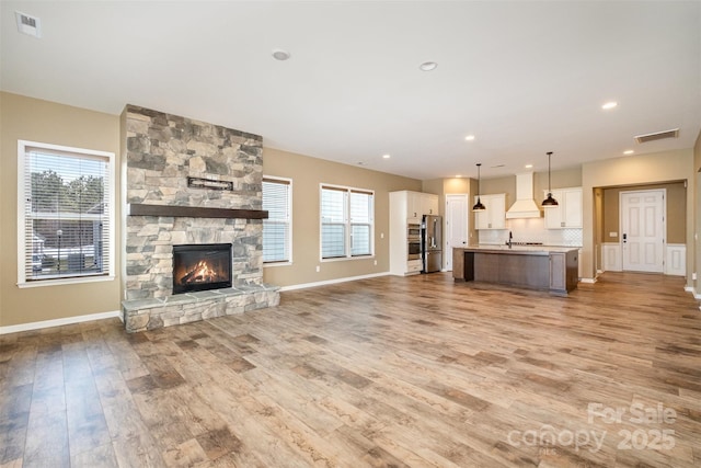 3105 Bonterra Blvd, Indian Trail, NC 28079 - unfurnished living room featuring light wood-type flooring, baseboards, a stone fireplace, a sink, and recessed lighting