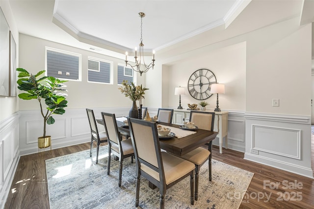 dining room featuring wood finished floors, crown molding, a chandelier, a decorative wall, and a wainscoted wall