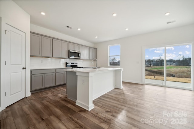 kitchen with gray cabinets, stainless steel appliances, dark wood-style floors, backsplash, and recessed lighting