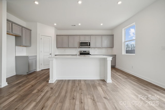 kitchen featuring stainless steel appliances, gray cabinets, light wood-style floors, a kitchen island with sink, and recessed lighting
