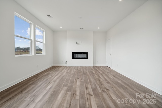 unfurnished living room featuring light wood-type flooring, a glass covered fireplace, recessed lighting, and baseboards