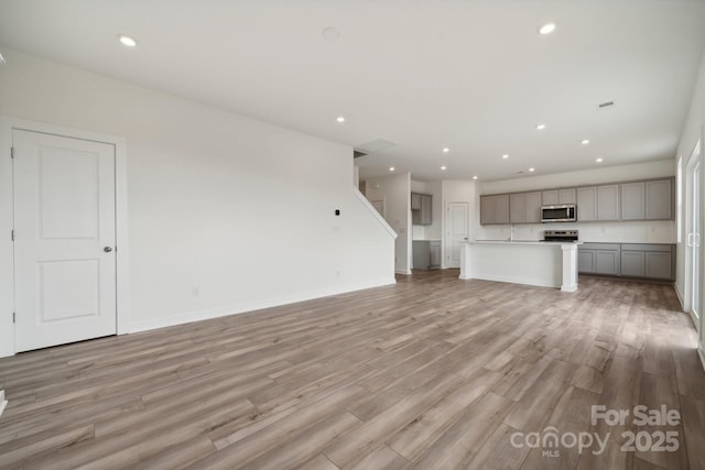 unfurnished living room with recessed lighting, light wood-type flooring, baseboards, and stairway