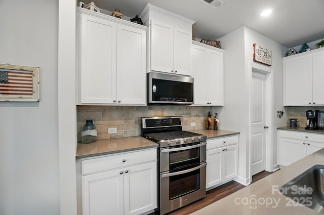 kitchen featuring appliances with stainless steel finishes, decorative backsplash, white cabinetry, dark wood finished floors, and recessed lighting