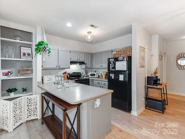 3308 Selwyn Farms Ln Unit 2, Charlotte, NC 28209 - kitchen with black appliances, a peninsula, light wood-type flooring, light countertops, and under cabinet range hood