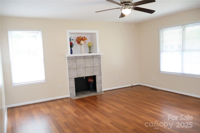 unfurnished living room with wood finished floors, ceiling fan, a tiled fireplace, and baseboards