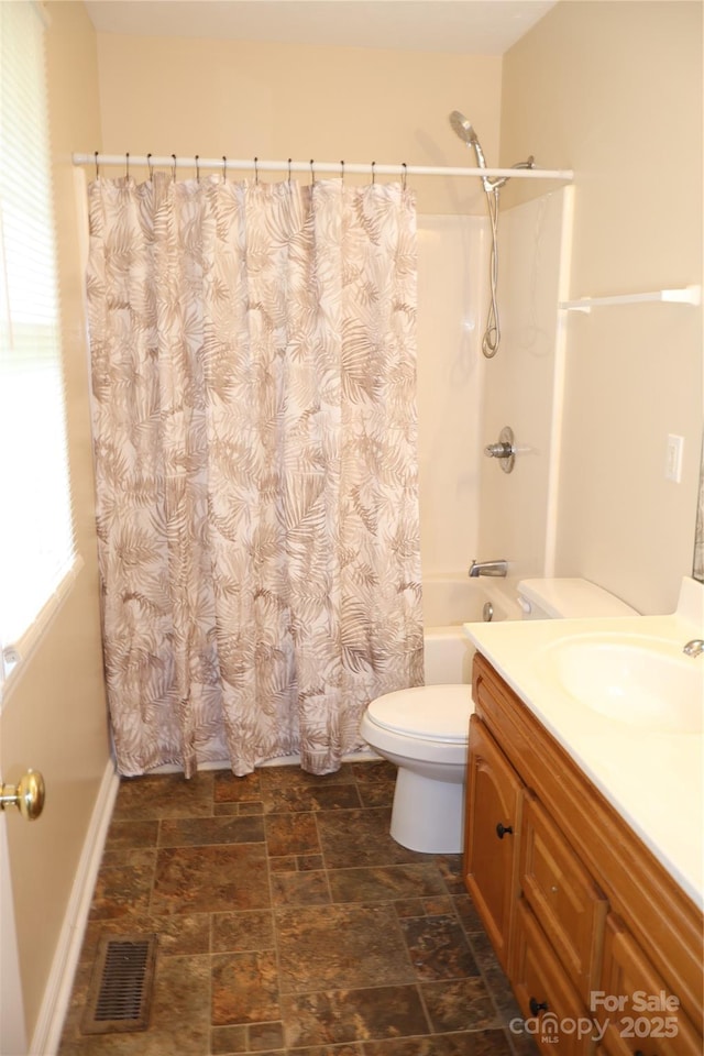 full bath featuring stone finish flooring, toilet, vanity, shower / tub combo, and baseboards