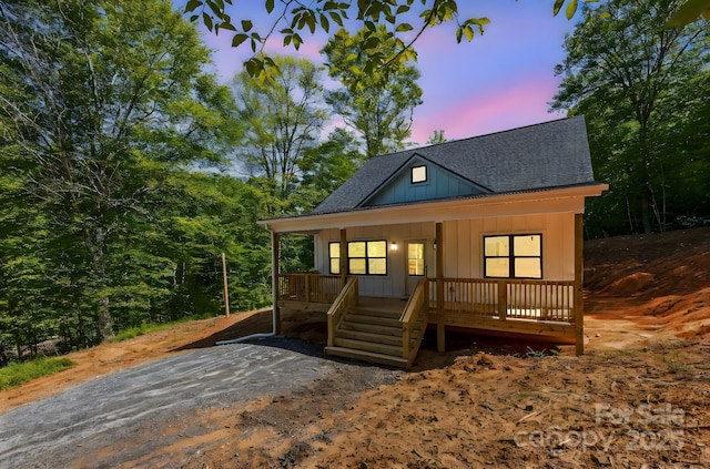 view of front of home featuring board and batten siding, a shingled roof, covered porch, and stairway