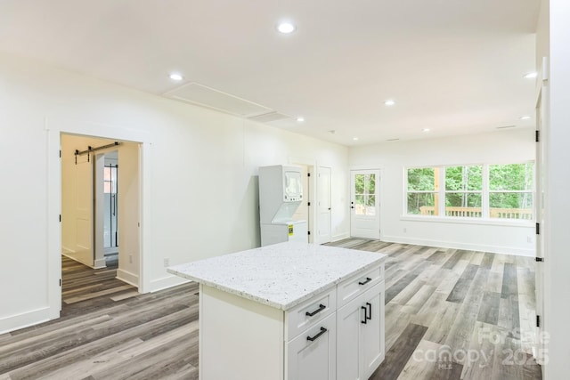 kitchen featuring stacked washing machine and dryer, light wood-style flooring, light stone counters, recessed lighting, and a kitchen island