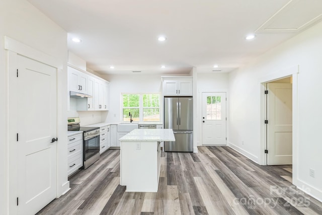 kitchen featuring appliances with stainless steel finishes, under cabinet range hood, wood finished floors, a center island, and white cabinets