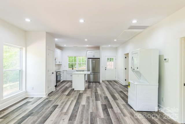 kitchen featuring appliances with stainless steel finishes, stacked washing machine and dryer, white cabinetry, a center island, and light countertops