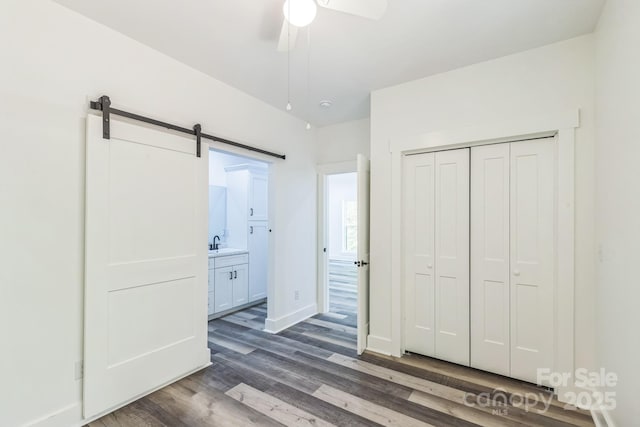 unfurnished bedroom featuring dark wood-style floors, a barn door, a sink, a closet, and a ceiling fan