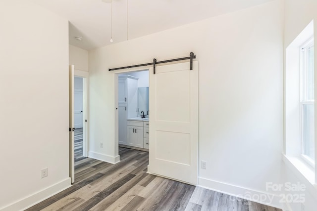 unfurnished bedroom featuring light wood-type flooring, a barn door, a sink, and connected bathroom