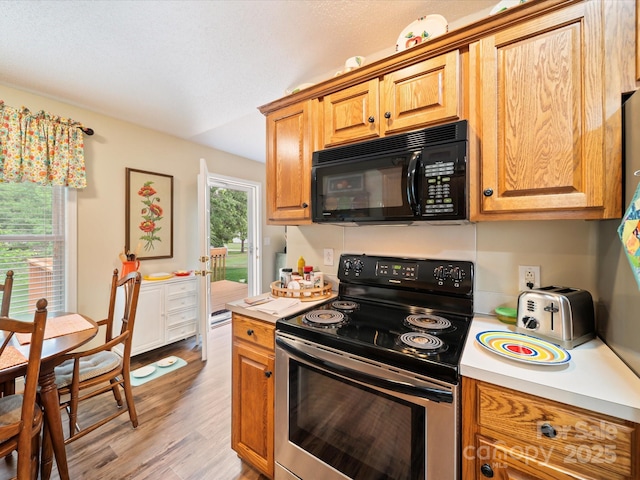 kitchen with black microwave, stainless steel range with electric stovetop, light countertops, light wood finished floors, and brown cabinetry