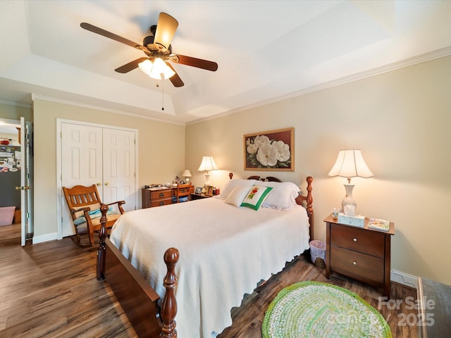 bedroom featuring a tray ceiling, dark wood-style flooring, ornamental molding, a closet, and a ceiling fan