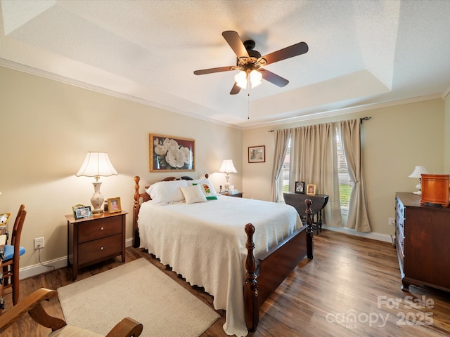 bedroom featuring a raised ceiling, wood finished floors, ornamental molding, baseboards, and a ceiling fan
