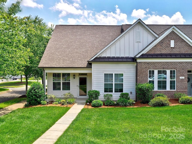 view of front of home with a front yard, board and batten siding, a shingled roof, a standing seam roof, and brick siding