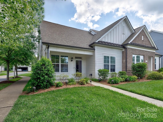 view of front of house with board and batten siding, a front yard, a shingled roof, and brick siding