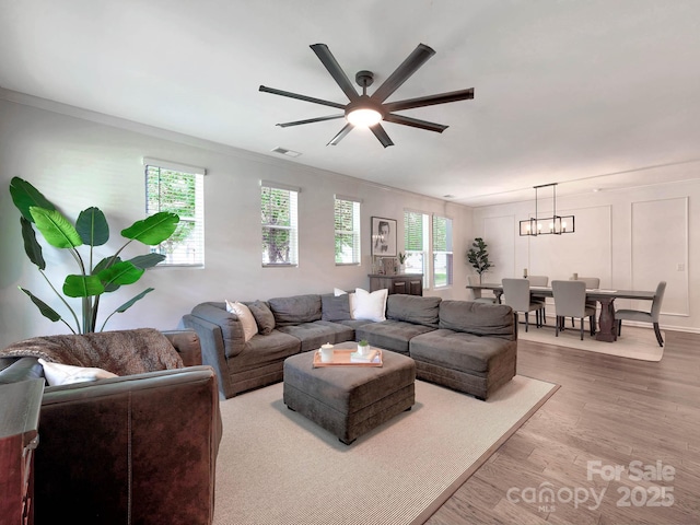 living area with ceiling fan, healthy amount of natural light, wood finished floors, crown molding, and a chandelier