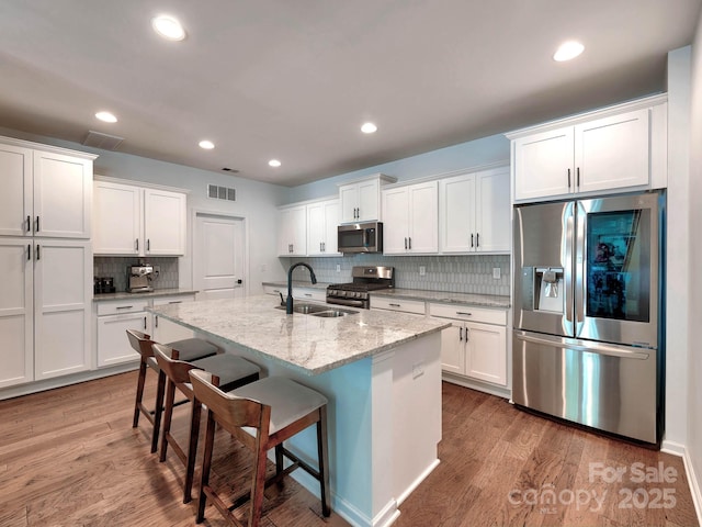 kitchen featuring appliances with stainless steel finishes, a sink, wood finished floors, white cabinets, and tasteful backsplash