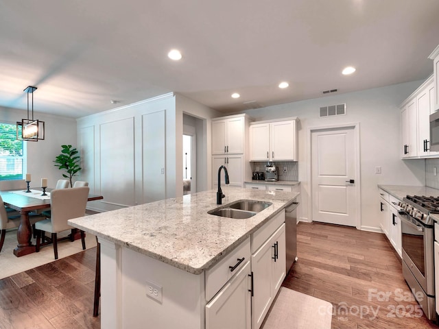 kitchen with a sink, appliances with stainless steel finishes, wood finished floors, white cabinets, and a center island with sink