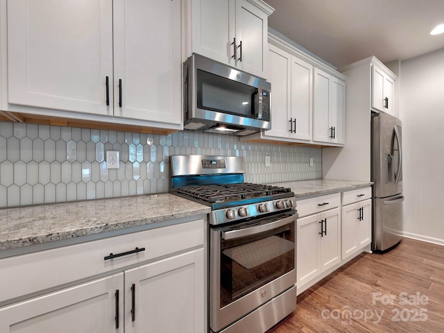 kitchen with stainless steel appliances, white cabinetry, light wood-type flooring, and backsplash