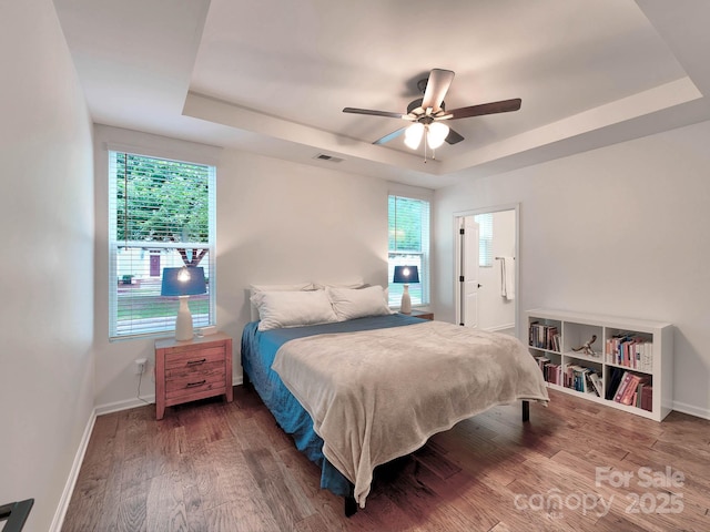 bedroom with a tray ceiling, wood finished floors, baseboards, and ceiling fan