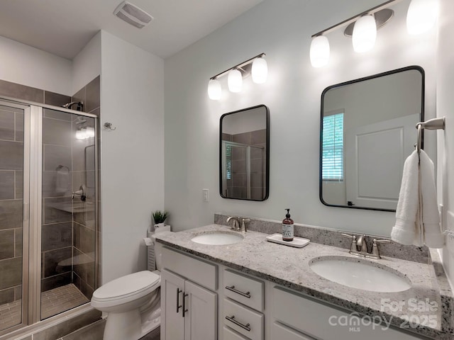 bathroom with a stall shower, toilet, and double vanity