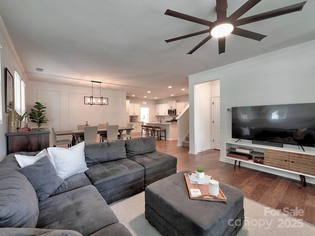 living area with wood finished floors, crown molding, ceiling fan, stairs, and recessed lighting