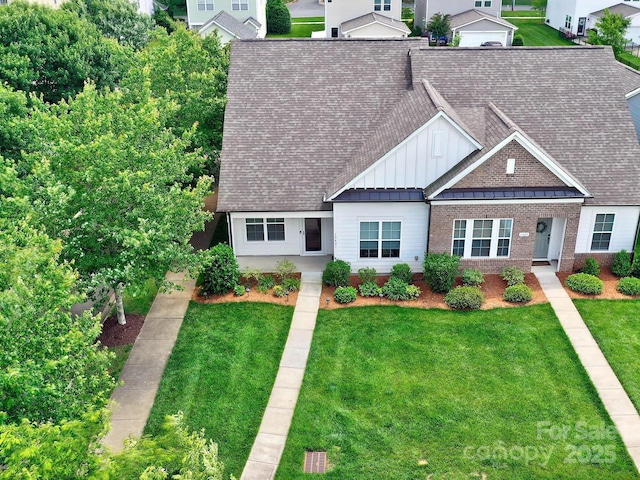 view of front of property with board and batten siding, roof with shingles, a front lawn, and brick siding