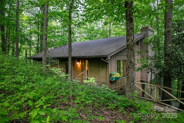 view of side of property with a chimney, a shingled roof, and board and batten siding