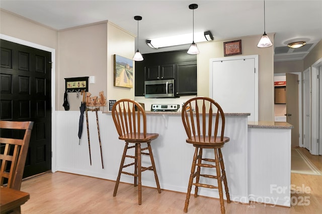 kitchen with stainless steel microwave, light wood-style floors, a kitchen breakfast bar, and range