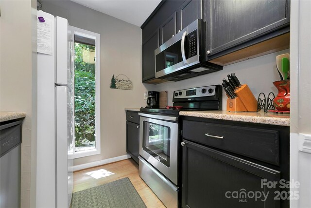 kitchen featuring appliances with stainless steel finishes, light wood-type flooring, dark cabinetry, and light stone counters