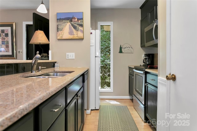 kitchen featuring appliances with stainless steel finishes, a sink, light wood finished floors, light stone countertops, and pendant lighting