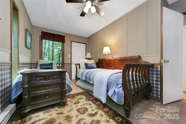 bedroom featuring wood finished floors, a decorative wall, and ceiling fan