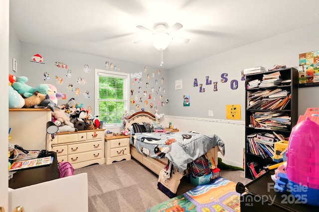 carpeted bedroom with ceiling fan and a wainscoted wall