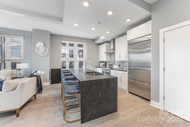 333 W Trade St Unit 1500, Charlotte, NC 28202 - kitchen featuring high end appliances, a sink, wall chimney range hood, dark countertops, and white cabinets