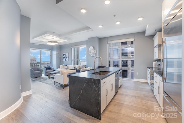 333 W Trade St Unit 1500, Charlotte, NC 28202 - kitchen featuring a sink, appliances with stainless steel finishes, an island with sink, a raised ceiling, and light wood finished floors