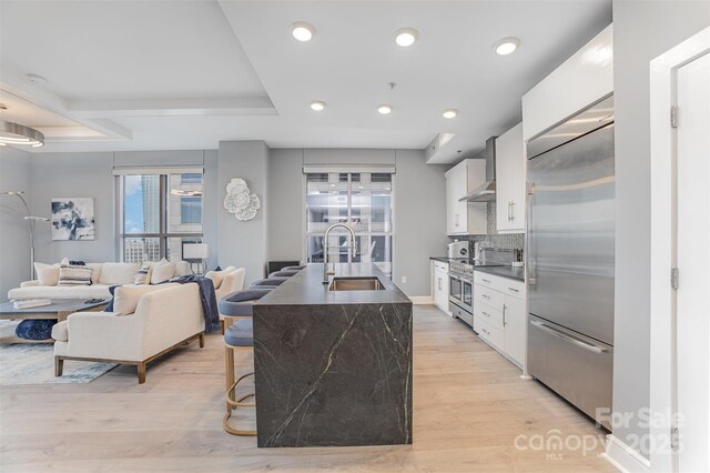 333 W Trade St Unit 1500, Charlotte, NC 28202 - kitchen with a sink, stainless steel appliances, dark countertops, wall chimney range hood, and white cabinetry