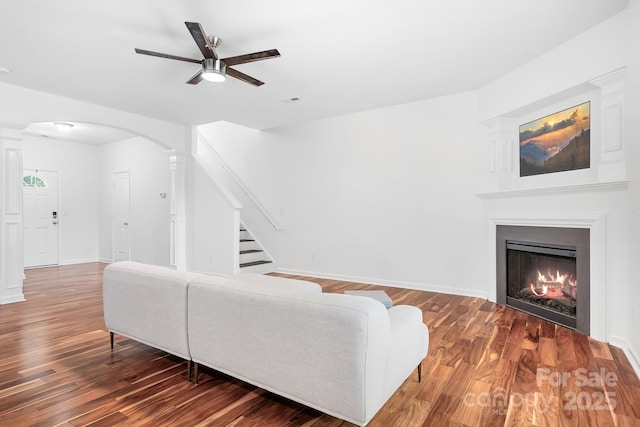 9437 Macquarie Ln, Charlotte, NC 28227 - living area featuring ceiling fan, arched walkways, wood finished floors, stairs, and a warm lit fireplace
