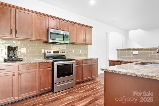 9437 Macquarie Ln, Charlotte, NC 28227 - kitchen featuring stainless steel appliances, ornate columns, a sink, light wood-type flooring, and decorative backsplash