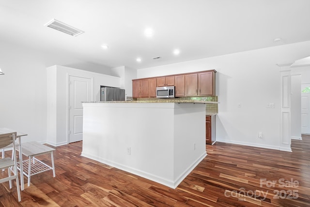 9437 Macquarie Ln, Charlotte, NC 28227 - kitchen featuring stainless steel appliances, dark wood-style floors, brown cabinetry, tasteful backsplash, and a center island with sink
