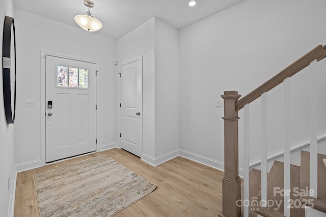 foyer entrance featuring stairs, light wood-style floors, and baseboards
