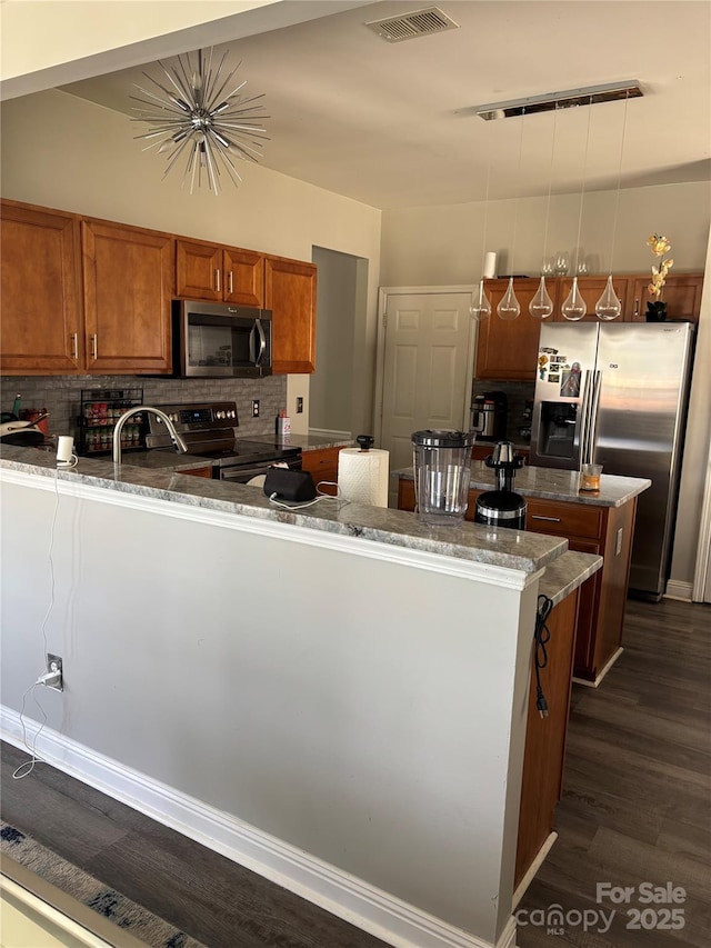 10826 Claude Freeman Dr, Charlotte, NC 28262 - kitchen featuring appliances with stainless steel finishes, brown cabinetry, a peninsula, and backsplash