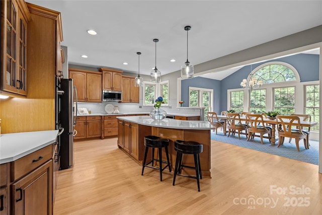 9021 Unbridle Ln, Waxhaw, NC 28173 - kitchen with appliances with stainless steel finishes, brown cabinets, a kitchen breakfast bar, light wood finished floors, and a kitchen island