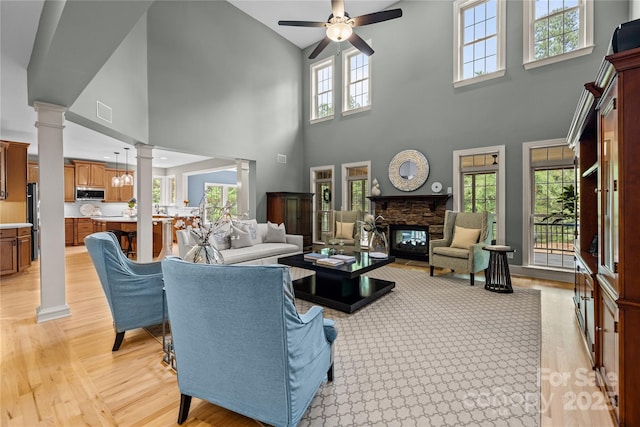 9021 Unbridle Ln, Waxhaw, NC 28173 - living area with decorative columns, a ceiling fan, a towering ceiling, light wood-style floors, and a stone fireplace