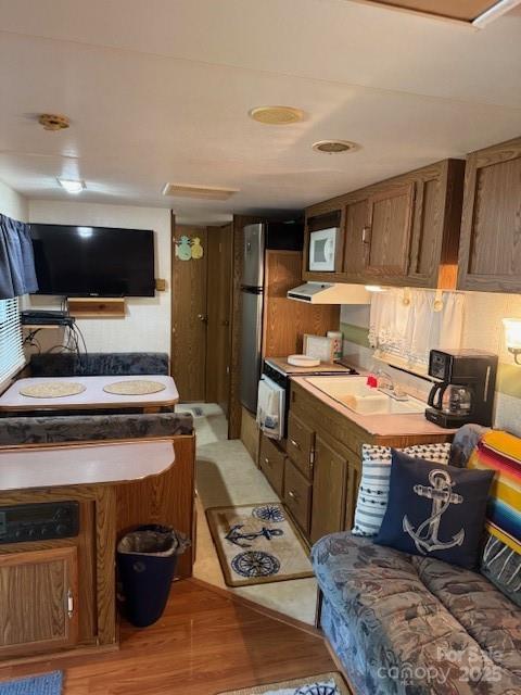 kitchen featuring light wood-type flooring, white microwave, a sink, brown cabinets, and range with electric stovetop