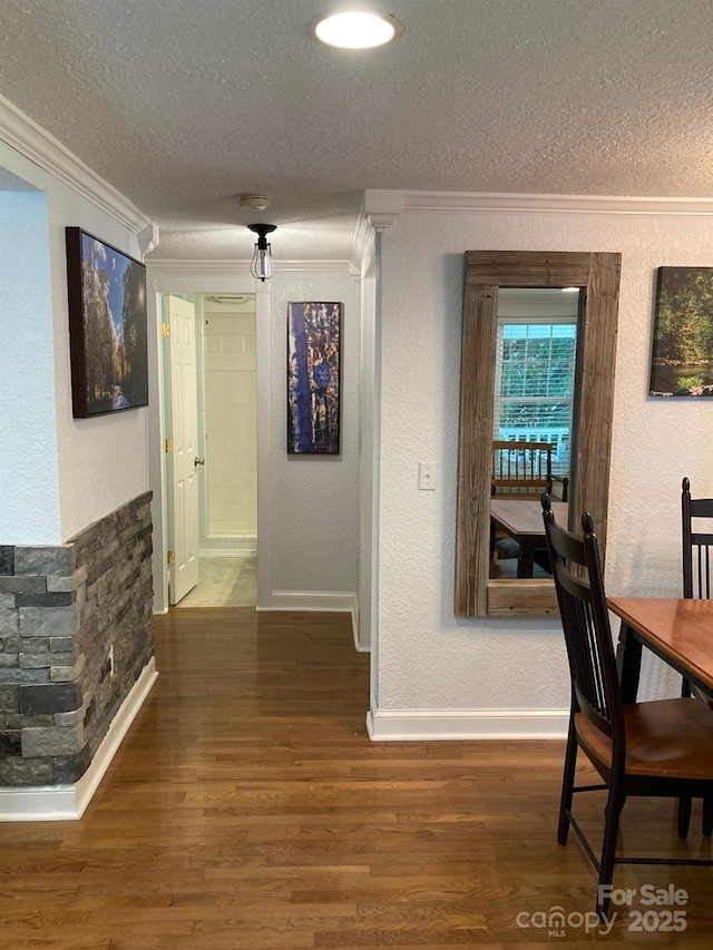 corridor featuring ornamental molding, a textured ceiling, a textured wall, wood finished floors, and baseboards